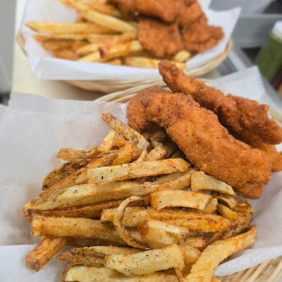 Basket of golden fried chicken tenders and seasoned thick-cut fries, with another serving of fries and tenders in the background.
